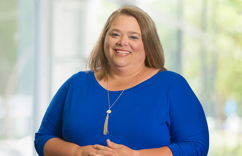 Portrait of LaCynda Brumbaugh, Senior Accountant at High Touch Technologies, standing and smiling in a bright office environment.