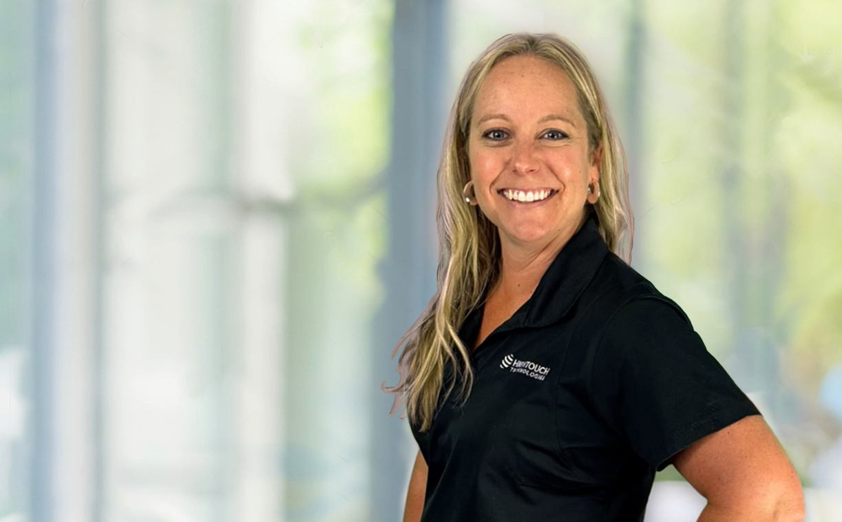 Lindsay Boxberger, Manager of Web and Custom Development at High Touch Technologies, smiling and wearing a branded black polo shirt, standing in front of a softly blurred office background.